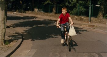 Movie still from “The Kid with a Bike” (2011), directed by Jean-Pierre Dardenne – A young boy riding a bike down a street; Wide shot, High angle