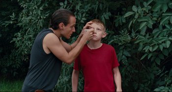 Movie still from “The Kid with a Bike” (2011), directed by Jean-Pierre Dardenne – A young man is putting makeup on a young boy's face; Close Up shot, Over the shoulder angle