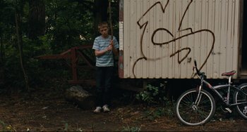 Movie still from “The Kid with a Bike” (2011), directed by Jean-Pierre Dardenne – A young boy standing in front of a shed with graffiti on it; Wide shot, Low angle