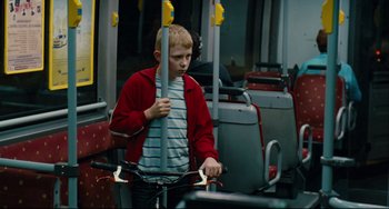 Movie still from “The Kid with a Bike” (2011), directed by Jean-Pierre Dardenne – A young boy riding a bike on a public transit bus; Medium shot, Over the shoulder angle