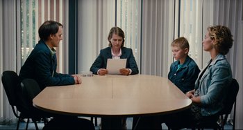 Movie still from “The Kid with a Bike” (2011), directed by Jean-Pierre Dardenne – Three people sitting at a table in front of a paper; Medium shot, Over the shoulder angle