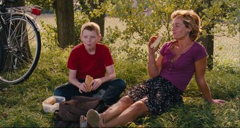 Movie still from “The Kid with a Bike” (2011), directed by Jean-Pierre Dardenne – A woman and a boy sitting in the grass eating hot dogs; Medium shot, Over the shoulder angle