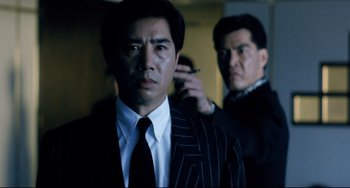 Movie still from “The Killer” (1989), directed by John Woo – A man in a suit and tie with a cigarette in his mouth; Close Up shot, Low angle