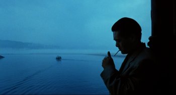 Movie still from “The Killer” (1989), directed by John Woo – A man smoking a cigarette in front of a body of water; Medium shot, High angle