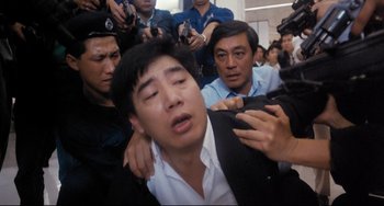 Movie still from “The Killer” (1989), directed by John Woo – A group of people surrounding a man with his hands on his chest; Close Up shot, High angle