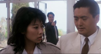 Movie still from “The Killer” (1989), directed by John Woo – A man and a woman are standing in front of another man holding a handgun; Close Up shot, Over the shoulder angle