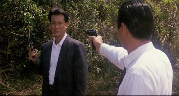 Movie still from “The Killer” (1989), directed by John Woo – A man holding a gun pointed at another man in front of him; Medium shot, Over the shoulder angle