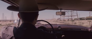 Movie still from “The Killer Inside Me” (2010), directed by Michael Winterbottom – A man in a cowboy hat is driving a car; Medium shot, Over the shoulder angle