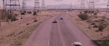 Movie still from “The Killer Inside Me” (2010), directed by Michael Winterbottom – Two cars driving down a road with power lines in the background; Extreme Wide shot, High angle