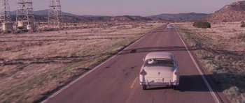 Movie still from “The Killer Inside Me” (2010), directed by Michael Winterbottom – A car driving down a road near a field; Extreme Wide shot, High angle