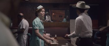 Movie still from “The Killer Inside Me” (2010), directed by Michael Winterbottom – A woman wearing a nurse's hat standing at a table; Medium shot, Over the shoulder angle