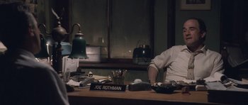 Movie still from “The Killer Inside Me” (2010), directed by Michael Winterbottom – A man sitting at a desk in front of a sign; Medium shot, Over the shoulder angle