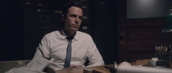 Movie still from “The Killer Inside Me” (2010), directed by Michael Winterbottom – A man sitting at a table in front of a stack of papers; Medium shot, Low angle
