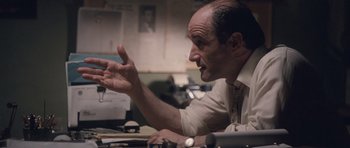 Movie still from “The Killer Inside Me” (2010), directed by Michael Winterbottom – A man sitting at a desk in front of papers; Medium shot, Over the shoulder angle