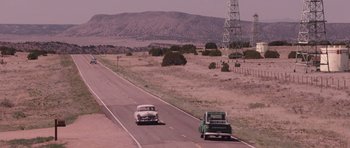 Movie still from “The Killer Inside Me” (2010), directed by Michael Winterbottom – Two vintage cars driving down a road in the middle of the desert; Extreme Wide shot, High angle