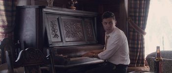 Movie still from “The Killer Inside Me” (2010), directed by Michael Winterbottom – A man in a white shirt and tie playing an old piano; Medium shot, Low angle