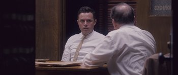 Movie still from “The Killer Inside Me” (2010), directed by Michael Winterbottom – A man wearing a white dress shirt and a tie talking to another man in front of him; Medium shot, Over the shoulder angle