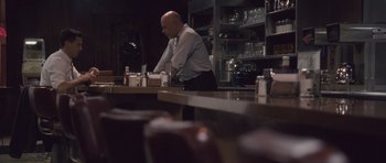 Movie still from “The Killer Inside Me” (2010), directed by Michael Winterbottom – A man standing at a counter in front of a counter; Wide shot, Over the shoulder angle