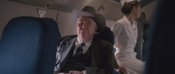 Movie still from “The Killer Inside Me” (2010), directed by Michael Winterbottom – An older man wearing a cowboy hat on an airplane; Medium shot, Over the shoulder angle