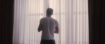 Movie still from “The Killer Inside Me” (2010), directed by Michael Winterbottom – A man standing in front of a window looking out at the sky; Medium shot, Low angle