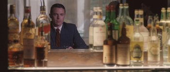 Movie still from “The Killer Inside Me” (2010), directed by Michael Winterbottom – A man sitting at a table with a glass of wine in front of him; Medium shot, Over the shoulder angle