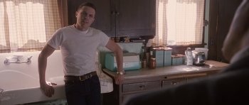 Movie still from “The Killer Inside Me” (2010), directed by Michael Winterbottom – A man standing in a kitchen next to a counter; Medium shot, Over the shoulder angle