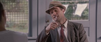 Movie still from “The Killer Inside Me” (2010), directed by Michael Winterbottom – A man in a suit and hat is smoking a cigarette; Medium shot, Low angle