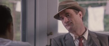 Movie still from “The Killer Inside Me” (2010), directed by Michael Winterbottom – A man in a suit and a hat is sitting in front of a door; Close Up shot, Over the shoulder angle
