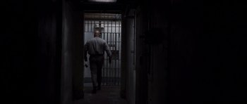 Movie still from “The Killer Inside Me” (2010), directed by Michael Winterbottom – A man walking through a dark hallway with a jail cell in the background; Wide shot, Low angle
