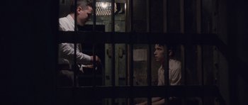 Movie still from “The Killer Inside Me” (2010), directed by Michael Winterbottom – Two men are sitting in a jail cell; Medium shot, High angle