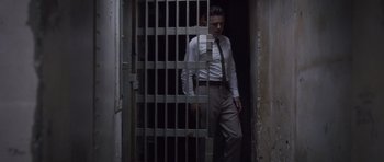 Movie still from “The Killer Inside Me” (2010), directed by Michael Winterbottom – A man in a suit and tie standing next to a jail cell; Wide shot, Low angle