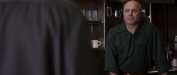 Movie still from “The Killer Inside Me” (2010), directed by Michael Winterbottom – A man sitting in front of a counter in a kitchen; Medium shot, Over the shoulder angle