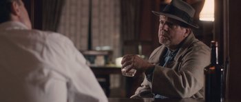 Movie still from “The Killer Inside Me” (2010), directed by Michael Winterbottom – An older man sitting at a table holding a glass; Medium shot, Over the shoulder angle