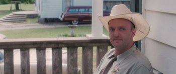 Movie still from “The Killer Inside Me” (2010), directed by Michael Winterbottom – A man in a cowboy hat and tie sitting on a porch; Close Up shot, Over the shoulder angle