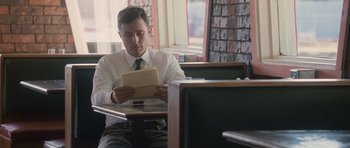 Movie still from “The Killer Inside Me” (2010), directed by Michael Winterbottom – A man sitting at a table reading a piece of paper; Medium shot, Over the shoulder angle