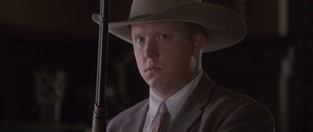 Movie still from “The Killer Inside Me” (2010), directed by Michael Winterbottom – A man in a suit and hat holding a rifle; Close Up shot, Low angle