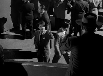 Movie still from “The Killers” (1946), directed by Robert Siodmak – Black and white photograph of a man in a suit and hat; Wide shot, High angle