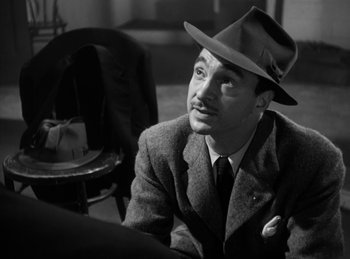 Movie still from “The Killers” (1946), directed by Robert Siodmak – A man wearing a suit and a hat sitting in a chair; Close Up shot, High angle