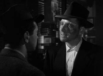 Movie still from “The Killers” (1946), directed by Robert Siodmak – A man in a hat and a suit talking to another man in a hat; Close Up shot, Over the shoulder angle