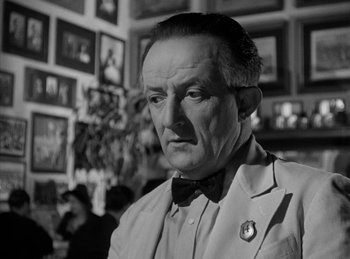 Movie still from “The Killers” (1946), directed by Robert Siodmak – An older man wearing a bow tie in a room; Close Up shot, Over the shoulder angle