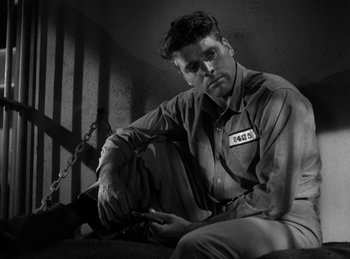 Movie still from “The Killers” (1946), directed by Robert Siodmak – A man sitting in a jail cell with chains around his ankles; Medium shot, Low angle