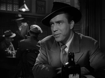 Movie still from “The Killers” (1946), directed by Robert Siodmak – A man in a suit and hat sitting at a table with a beer; Medium shot, Over the shoulder angle
