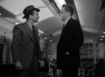 Movie still from “The Killers” (1946), directed by Robert Siodmak – Two men in suits talking to each other in a train station; Medium shot, Low angle