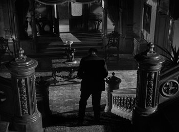 Movie still from “The Killers” (1946), directed by Robert Siodmak – A man in a suit standing in front of a staircase; Wide shot, High angle