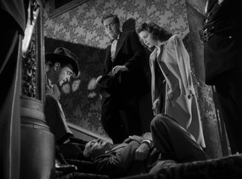 Movie still from “The Killers” (1946), directed by Robert Siodmak – A group of people standing around in a room; Wide shot, Overhead angle