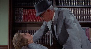 Movie still from “The Killers” (1964), directed by Don Siegel – A man in a suit and a hat touching the head of a woman in a suit; Medium shot, Low angle