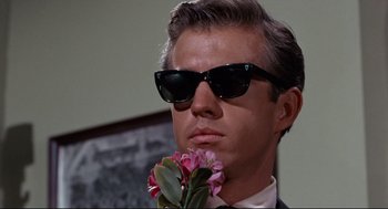 Movie still from “The Killers” (1964), directed by Don Siegel – A person wearing sunglasses and holding a flower; Close Up shot, Low angle