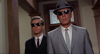 Movie still from “The Killers” (1964), directed by Don Siegel – A man in a suit and a man in a hat and sunglasses; Close Up shot, Low angle