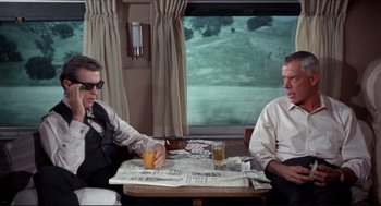 Movie still from “The Killers” (1964), directed by Don Siegel – Two men sitting at a table with a newspaper and a glass of orange juice in front of them; Medium shot, Over the shoulder angle