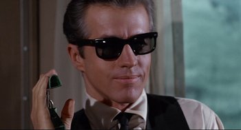 Movie still from “The Killers” (1964), directed by Don Siegel – A person wearing a suit and sunglasses; Close Up shot, Low angle